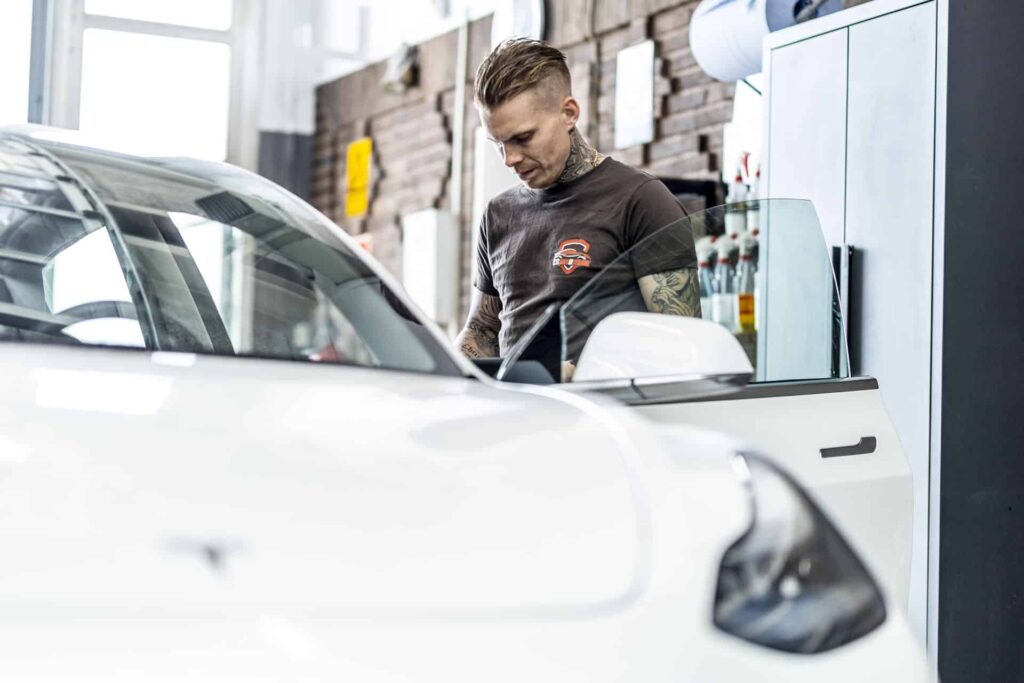 automekaniker fra CS Autoteknik står på værksted ved hvid bil med åben sidedør