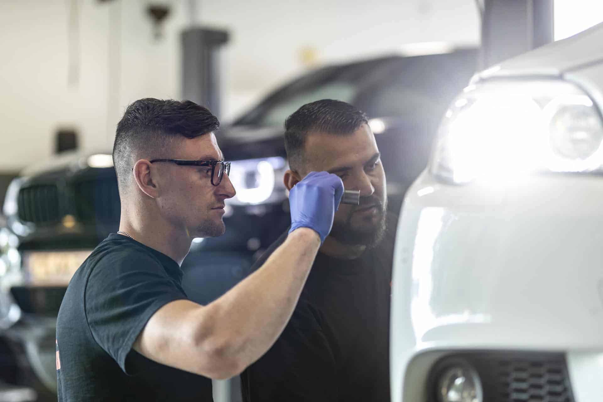 to mekanikere fra CS Autoteknik kigger på bil mens den ene lyser med lommelygte