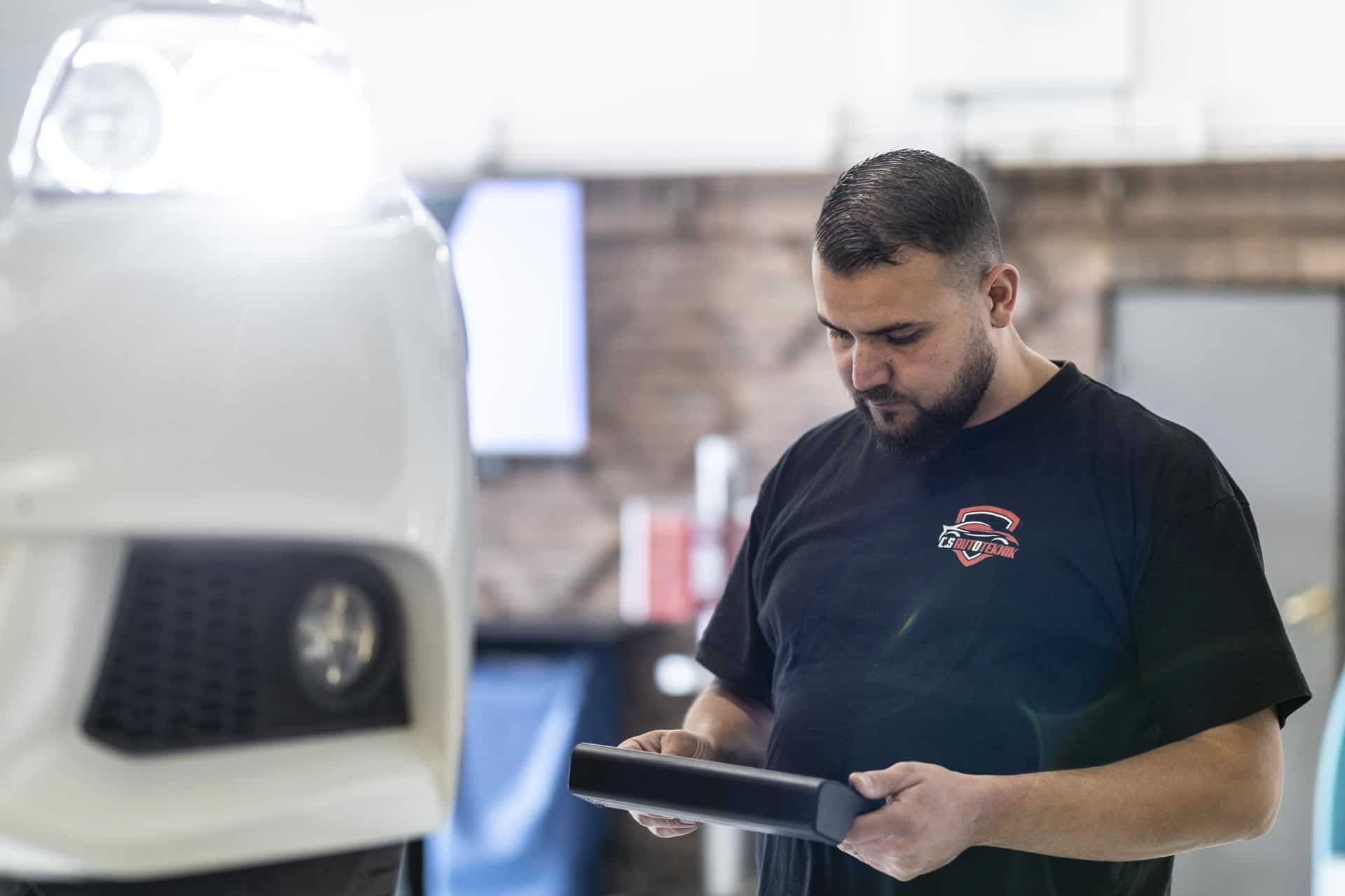 CS Autoteknik-mekaniker kigger på et display ved siden af hvid bil på lift
